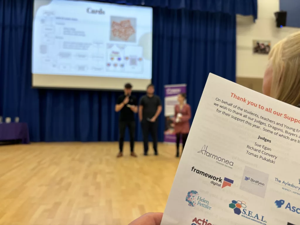 a blurred image of students presenting in the background with a leaflet including Framework Digital logo in the foreground.