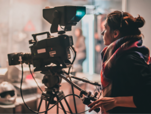 A Woman in a film set holding a film camera with dark lighting.